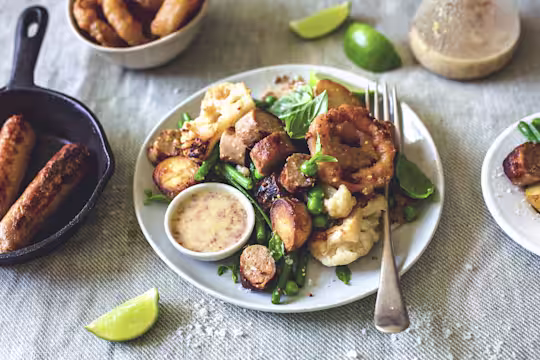 A plate of salad of warm Quorn sausage crispy baby potatoes, peas and grean beens with Mustard and Lime vinaigrette