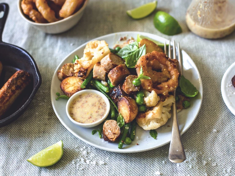 A plate of salad of warm Quorn sausage crispy baby potatoes, peas and grean beens with Mustard and Lime vinaigrette