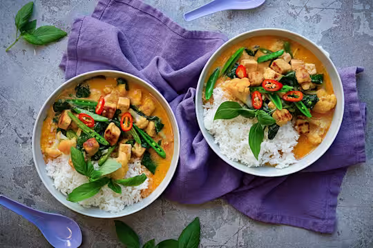 Kaksi kulhoa Thai Currya Quorn Kuutioilla. Päällä vihreitä kasviksia ja punaista chiliä. Tarjoillaan riisin kera.