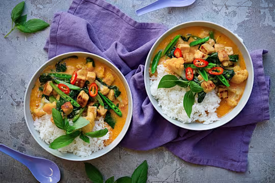 Kaksi kulhoa Thai Currya Quorn Kuutioilla. Päällä vihreitä kasviksia ja punaista chiliä. Tarjoillaan riisin kera.