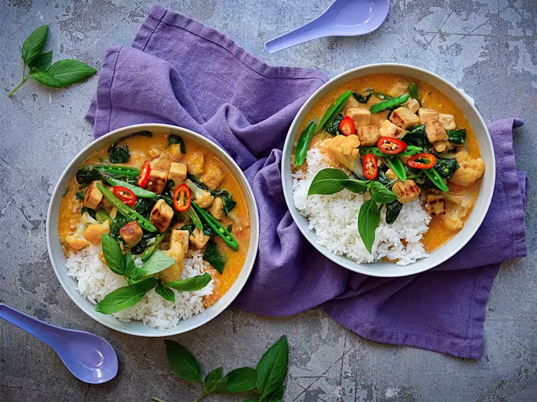 Kaksi kulhoa Thai Currya Quorn Kuutioilla. Päällä vihreitä kasviksia ja punaista chiliä. Tarjoillaan riisin kera.