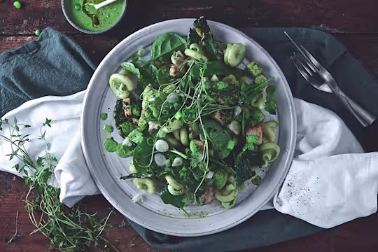 A plate of green vegan pesto pasta made with Quorn Vegan Pieces on top of a dark blue napkin and white napkin