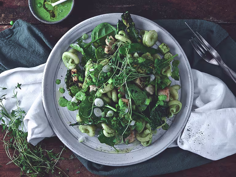 A plate of green vegan pesto pasta made with Quorn Vegan Pieces on top of a dark blue napkin and white napkin