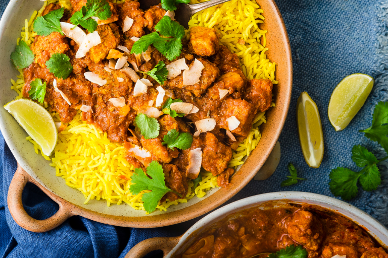 A vegetarian rogan josh curry made with Quorn Pieces topped with dried coconut and coriander atop a bed of saffron rice with a wedge of lemon on the side.