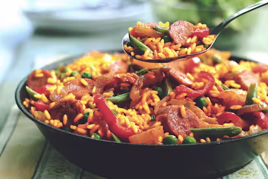A spoon full of vegetarian paella held over a bowl of the vegetarian paella.
