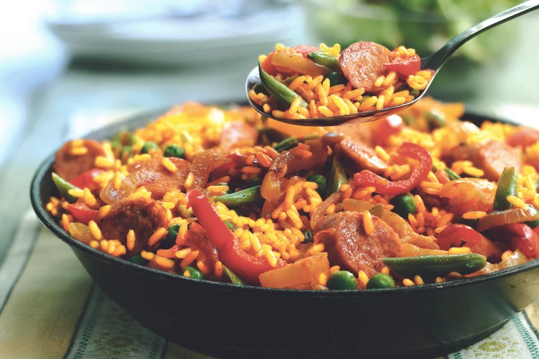 A spoon full of vegetarian paella held over a bowl of the vegetarian paella. 