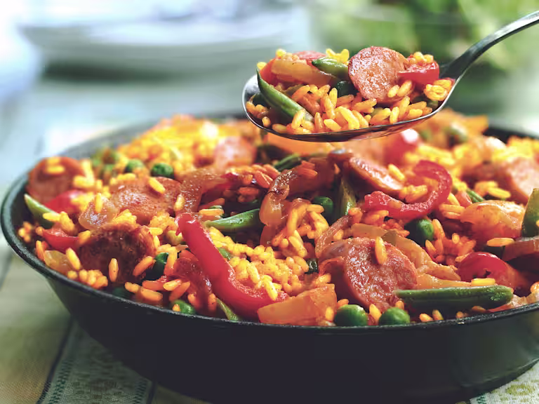 A spoon full of vegetarian paella held over a bowl of the vegetarian paella.