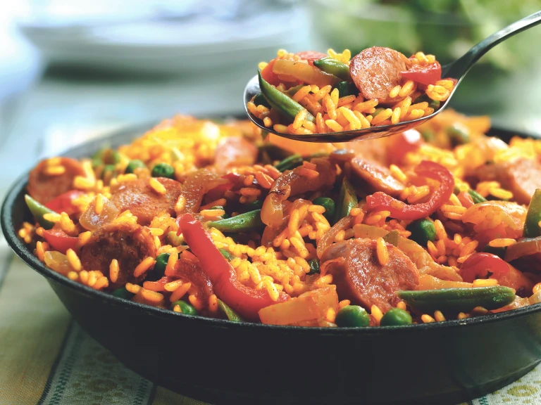 A spoon full of vegetarian paella held over a bowl of the vegetarian paella. 