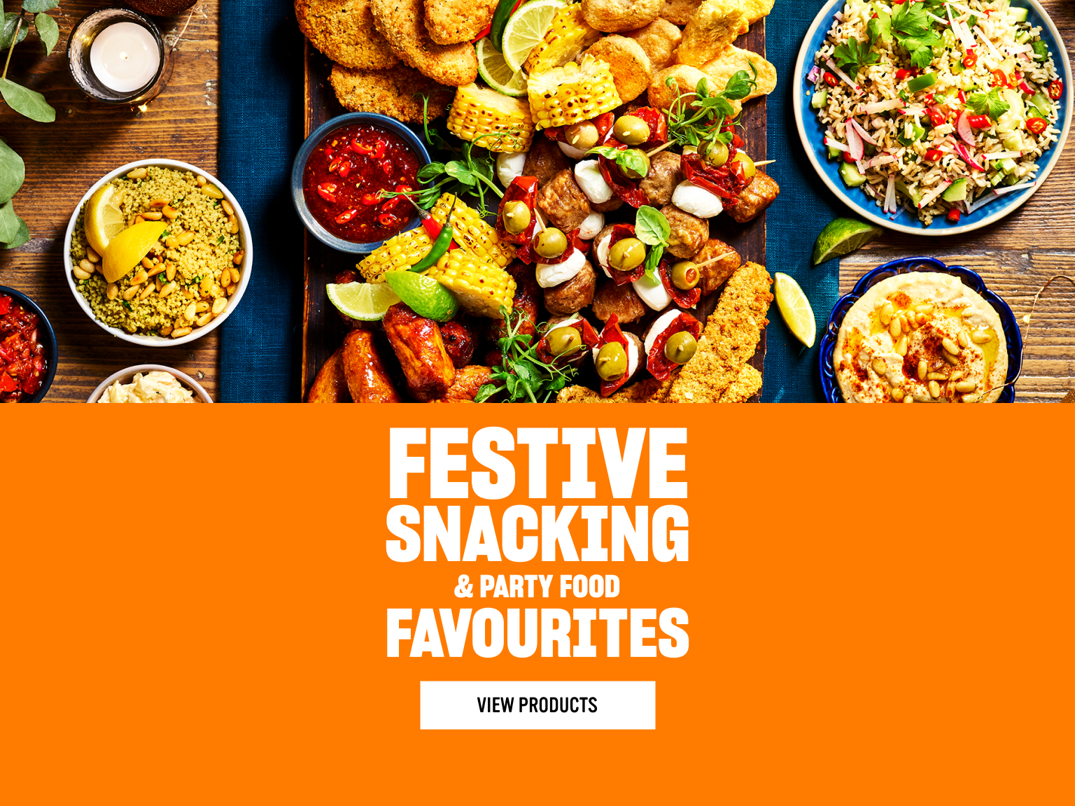 A colourful festive party food spread with quorns snacking products, sausages, dips, couscous, salad and hummus on a wooden table, beside bold orange text reading ‘Festive Snacking & Party Food Favourites’ and a button labelled ‘View Products.