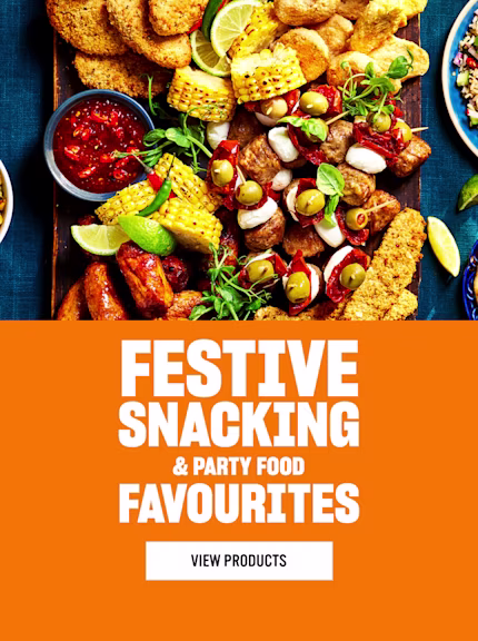 A colourful festive party food spread with quorns snacking products, sausages, dips, couscous, salad and hummus on a wooden table, beside bold orange text reading ‘Festive Snacking & Party Food Favourites’ and a button labelled ‘View Products.