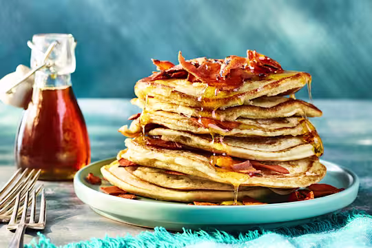 Stack of pancakes served on a white plate drizzled in maple syrup