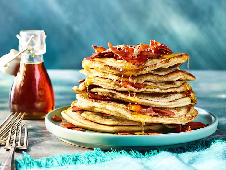 Stack of pancakes served on a white plate drizzled in maple syrup