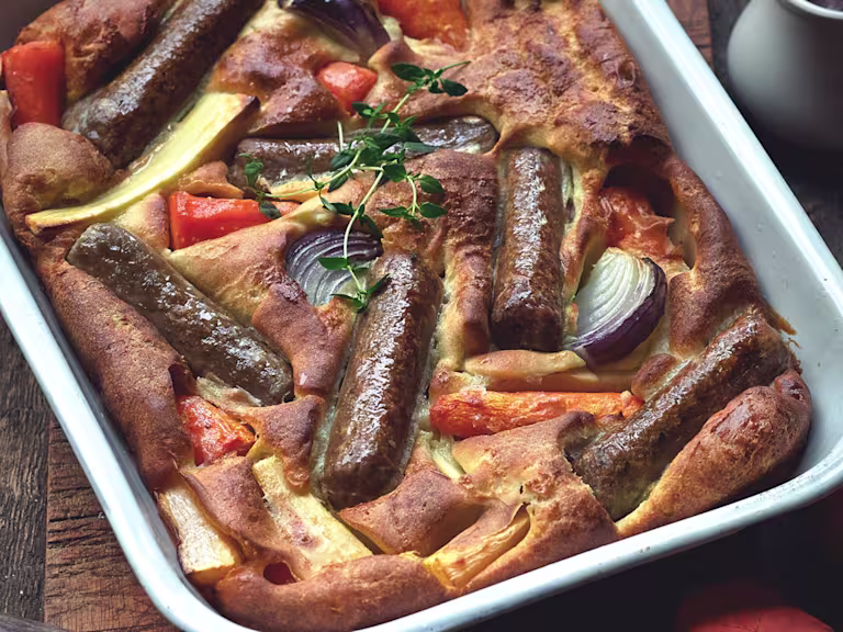 Toad in the hole recipe made with Quorn sausages and root vegetables served in a roasting tin topped with a sprig of thyme