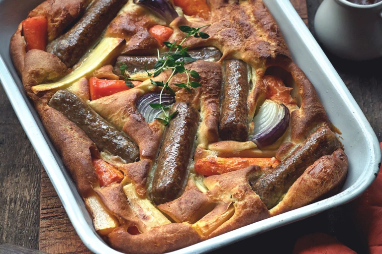 Toad in the hole recipe made with Quorn sausages and root vegetables served in a roasting tin topped with a sprig of thyme