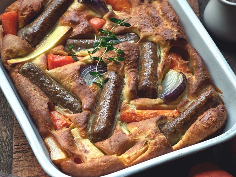 Toad in the hole recipe made with Quorn sausages and root vegetables served in a roasting tin topped with a sprig of thyme