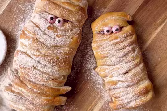 Strips of pizza dough wrapped in a mummy shape with googly eyes and dusted with flour.