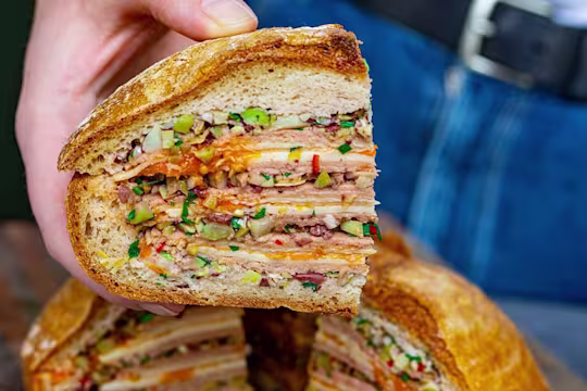 Someone holding a slice of vegetarian Muffaletta layered with Quorn vegetarian ham and cheese with tomato jam.
