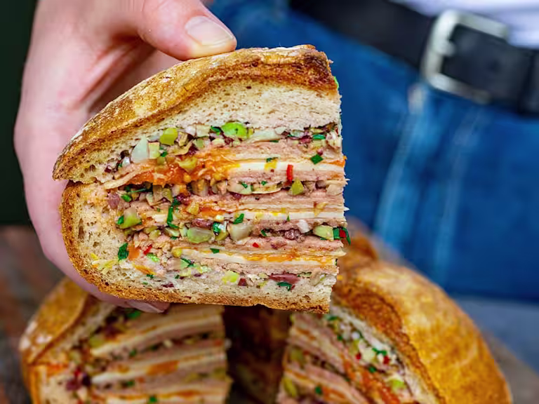 Someone holding a slice of vegetarian Muffaletta layered with Quorn vegetarian ham and cheese with tomato jam.