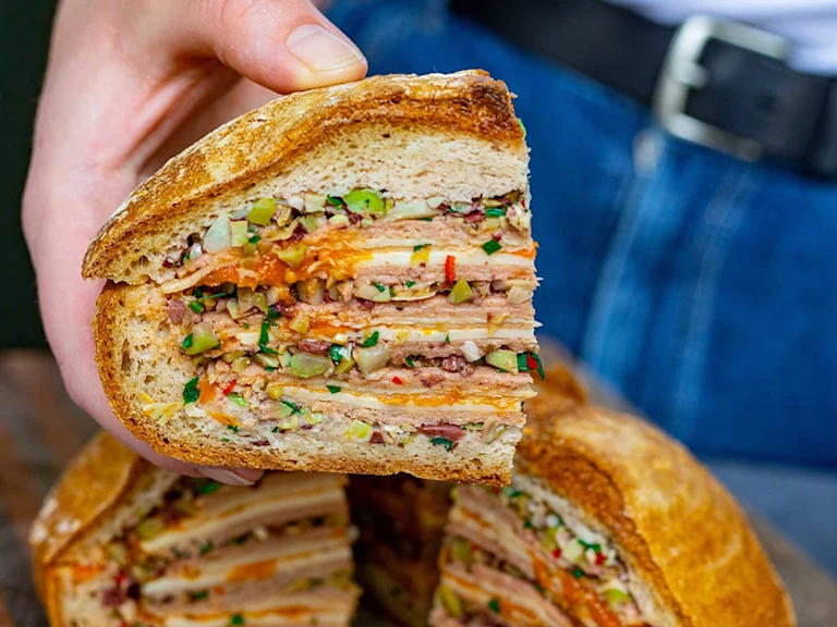 Someone holding a slice of vegetarian Muffaletta layered with Quorn vegetarian ham and cheese with tomato jam.