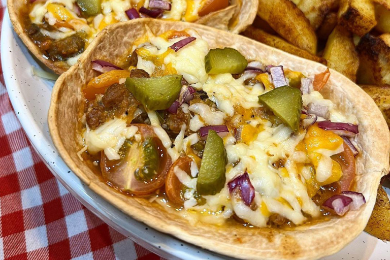 Quorn mince filling in a taco boat topped with melted cheese, gherkins, red onion and cherry tomatoes.