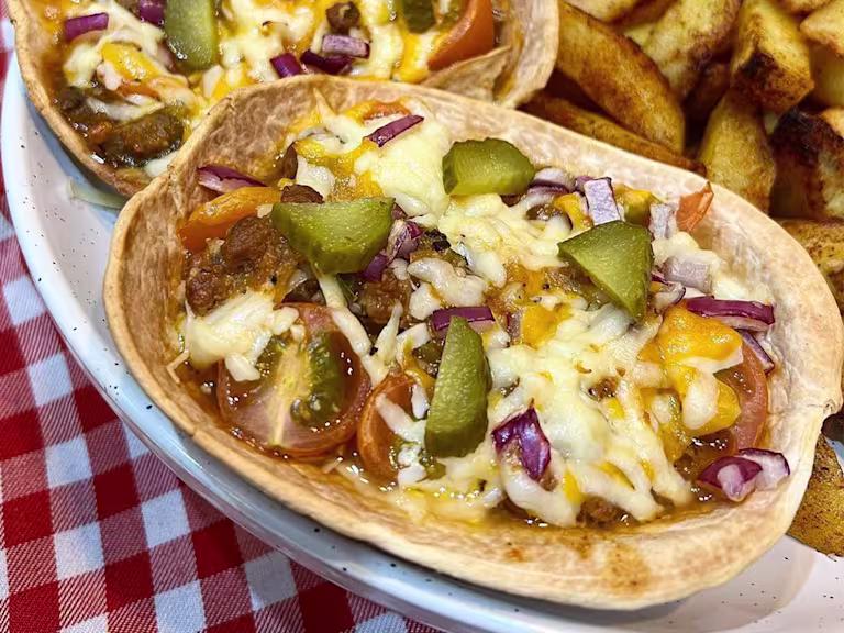 Quorn mince filling in a taco boat topped with melted cheese, gherkins, red onion and cherry tomatoes.