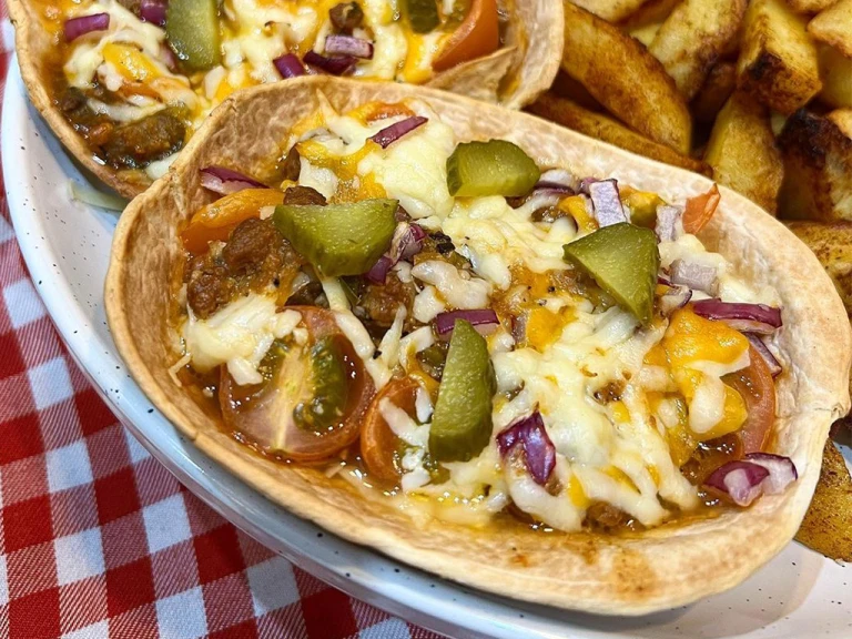 Quorn mince filling in a taco boat topped with melted cheese, gherkins, red onion and cherry tomatoes.