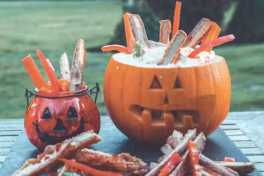 Easy snacks of Quorn Sausages and Quorn Sweet and Smoky Strips sitting in hummus, served in a carved pumpkin and glass pumpkin
