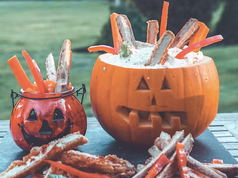 Easy snacks of Quorn Sausages and Quorn Sweet and Smoky Strips sitting in hummus, served in a carved pumpkin and glass pumpkin