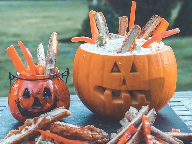 Easy snacks of Quorn Sausages and Quorn Sweet and Smoky Strips sitting in hummus, served in a carved pumpkin and glass pumpkin