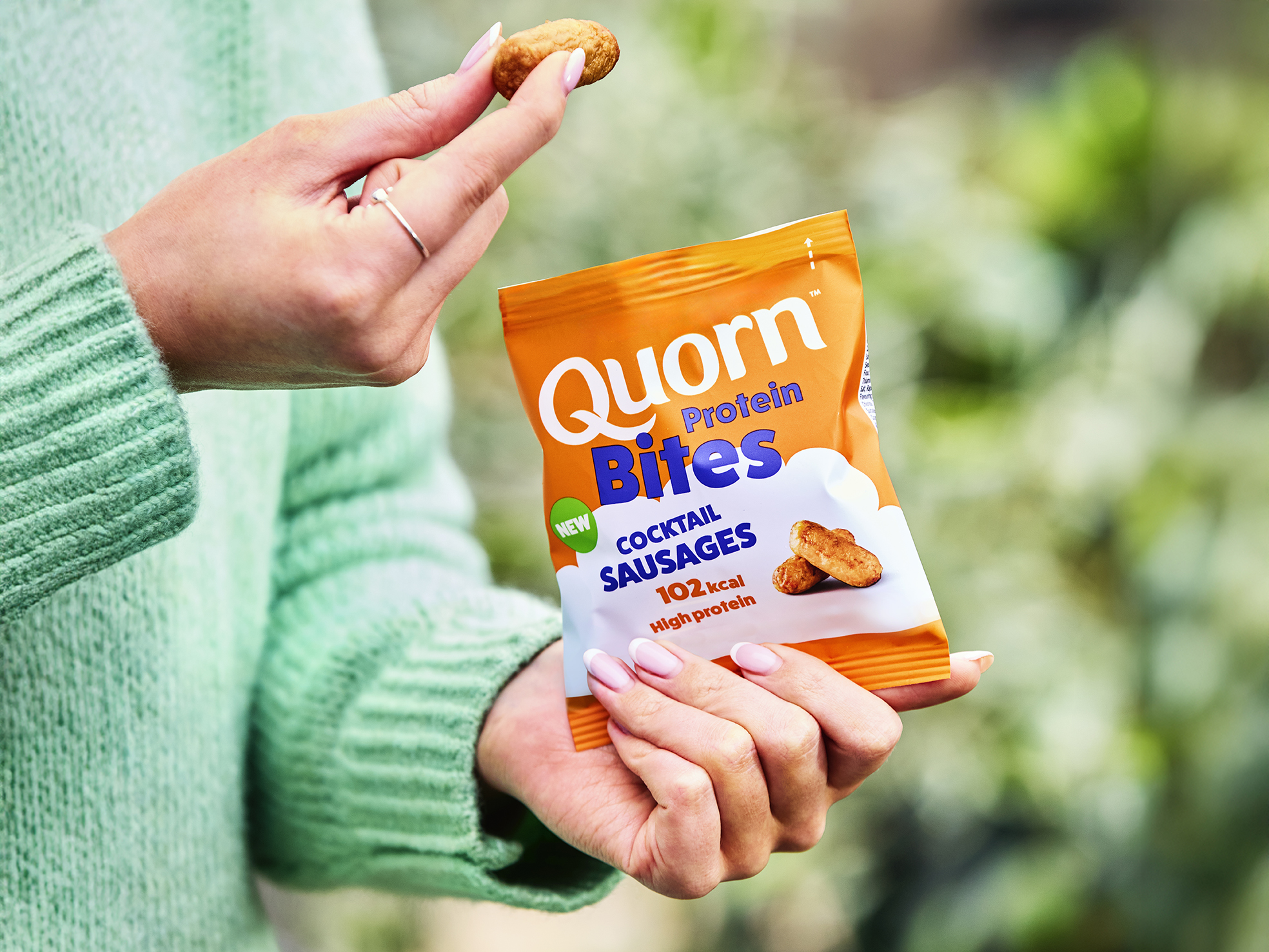 Quorn Protein Bites Cocktail Sausages in a hand infront of green nature scene 