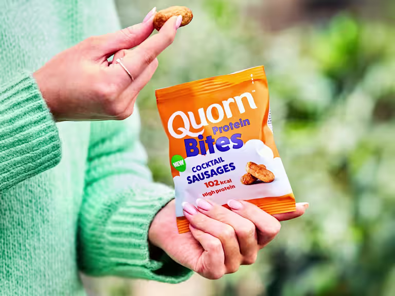 Quorn Protein Bites Cocktail Sausages in a hand infront of green nature scene
