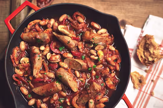 Vegetarian sausage casserole in a black skillet with mushrooms, beans, pepper and tomato sauce.