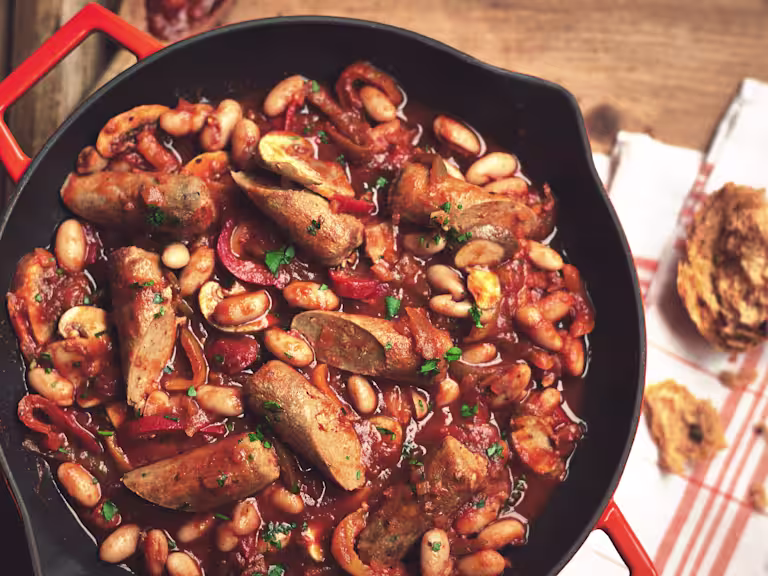 Vegetarian sausage casserole in a black skillet with mushrooms, beans, pepper and tomato sauce.