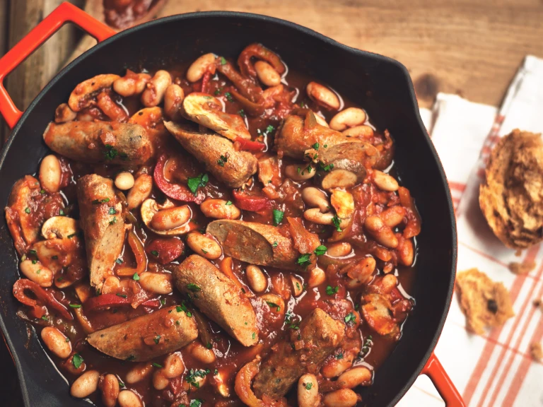 A casserole made with Quorn Sausages, beans, and peppers in a shallow Dutch oven.