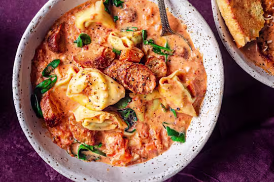 Vegetarian sausage and tortellini soup served in a white bowl with Quorn Cocktail Sausages on the side.