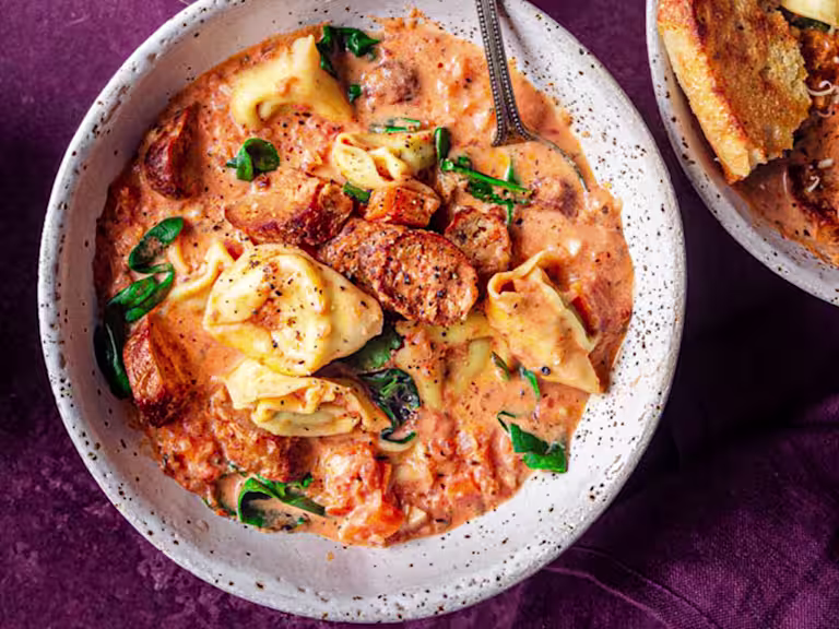 Vegetarian sausage and tortellini soup served in a white bowl with Quorn Cocktail Sausages on the side.