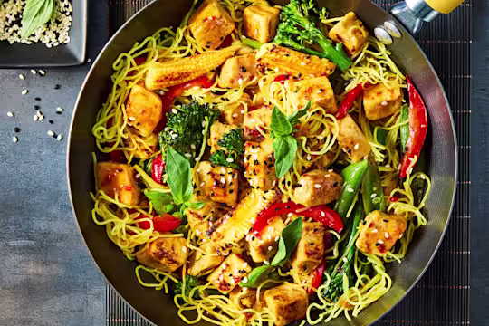 Quorn Chicken Pieces in a stir fry with noodles, chopped pepper, tenderstem broccoli and baby sweetcorn in a wok.