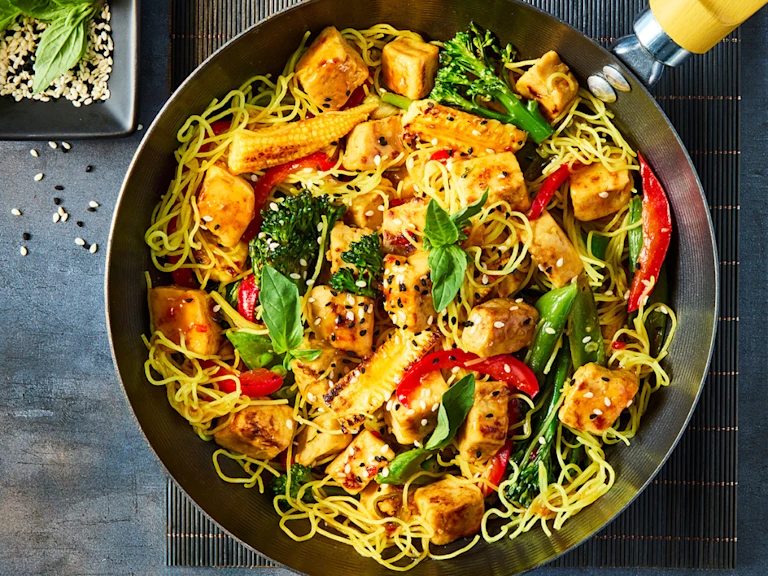 Quorn Chicken Pieces in a stir fry with noodles, chopped pepper, tenderstem broccoli and baby sweetcorn in a wok.