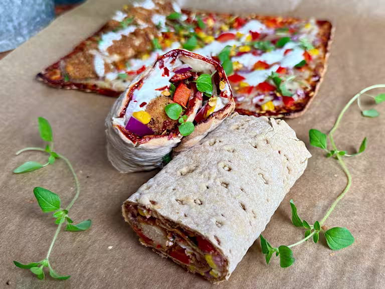 Vegetariska pizzarullar gjorda på tunnbröd, fyllda med Quorn Salt & Pepper Tenders, paprika, rödlök, majs och ost, toppade med färsk oregano. I bakgrunden syns en platt pizza med samma fyllning på bakplåtspapper.