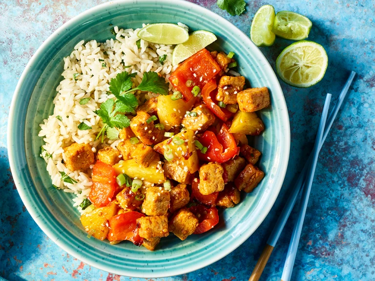 Hawaiian BBQ bowl with Quorn pieces served in a blue bowl with blue chopsticks and limes on the side.