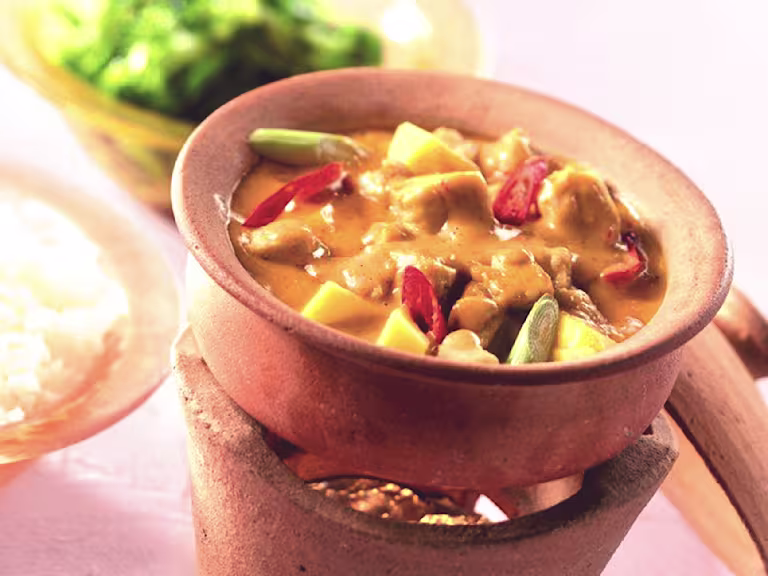 Vegetarian Thai red curry made with Quorn Pieces, peppers and mango served in a ceramic dish next to a bowl of rice