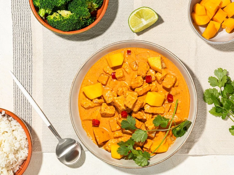 A red curry with lemongrass, mango, and Quorn Pieces in a terra cotta bowl with a bowl of rice on the side.