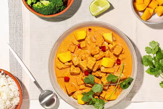 A red curry with lemongrass, mango, and Quorn Pieces in a terra cotta bowl with a bowl of rice on the side.