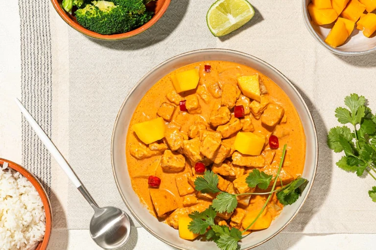 A red curry with lemongrass, mango, and Quorn Pieces in a terra cotta bowl with a bowl of rice on the side.