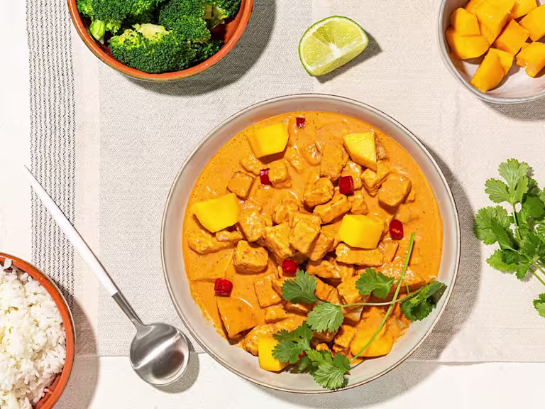 A red curry with lemongrass, mango, and Quorn Pieces in a terra cotta bowl with a bowl of rice on the side.