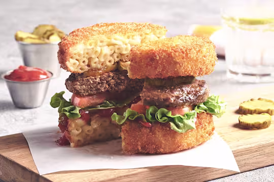 Vegetarian Mac and Cheese Bun Burger, made with Quorn Quarter Pounders, tomato, lettuce, fried mac and cheese, served in a burger bun on a plate.