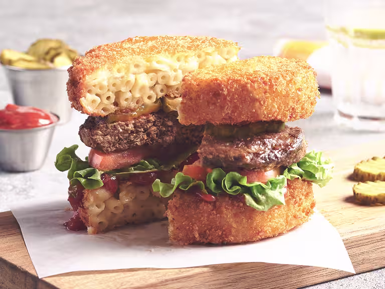Vegetarian Mac and Cheese Bun Burger, made with Quorn Quarter Pounders, tomato, lettuce, fried mac and cheese, served in a burger bun on a plate.