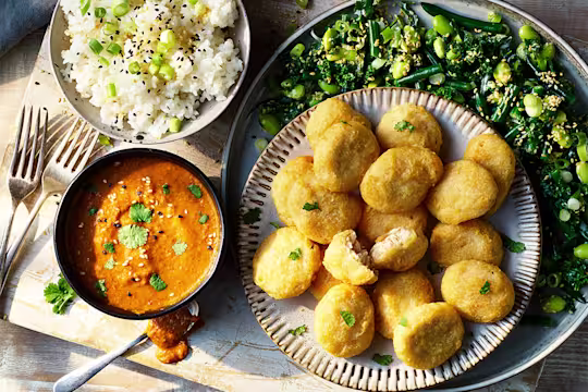 A plate of Quorn Meatless ChiQin Nuggets served alongside a bowl of sushi rice and katsu curry sauce on top of a plate of green vegetables.