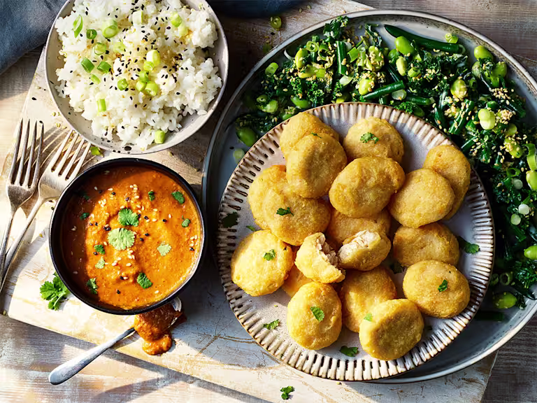 A plate of Quorn Meatless ChiQin Nuggets served alongside a bowl of sushi rice and katsu curry sauce on top of a plate of green vegetables.