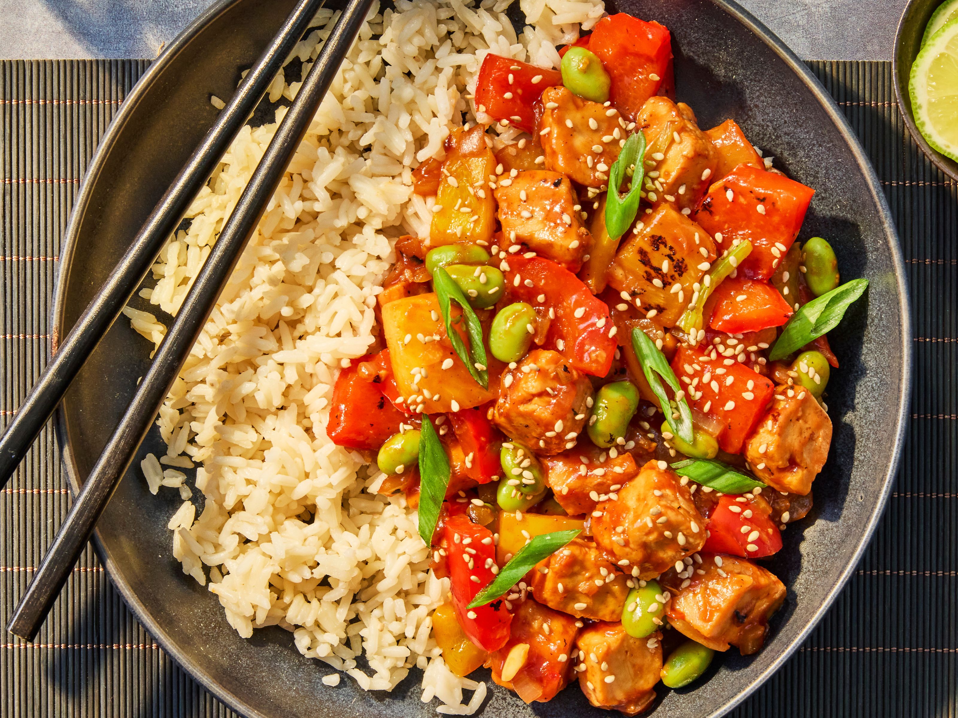 Quorn sweet and sour, served with Quorn Pieces, lime wedges on a plate with chopsticks on top.
